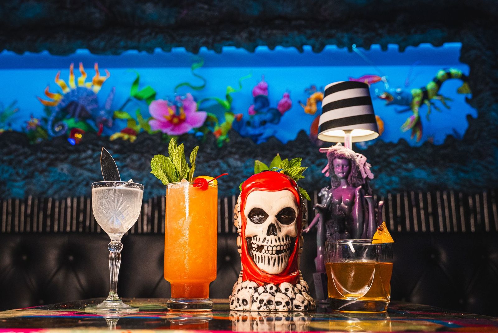 Three cocktails and a skull mug under blacklight at Endless Bummer