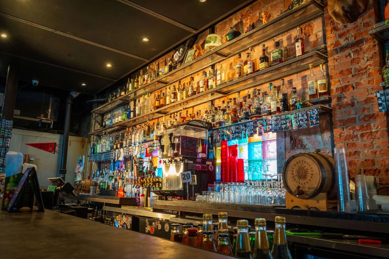 The back bar at Betelgeuse Betelgeuse Montrose: lit shelves of spirits on a brick wall and a Betelgeuse barrel