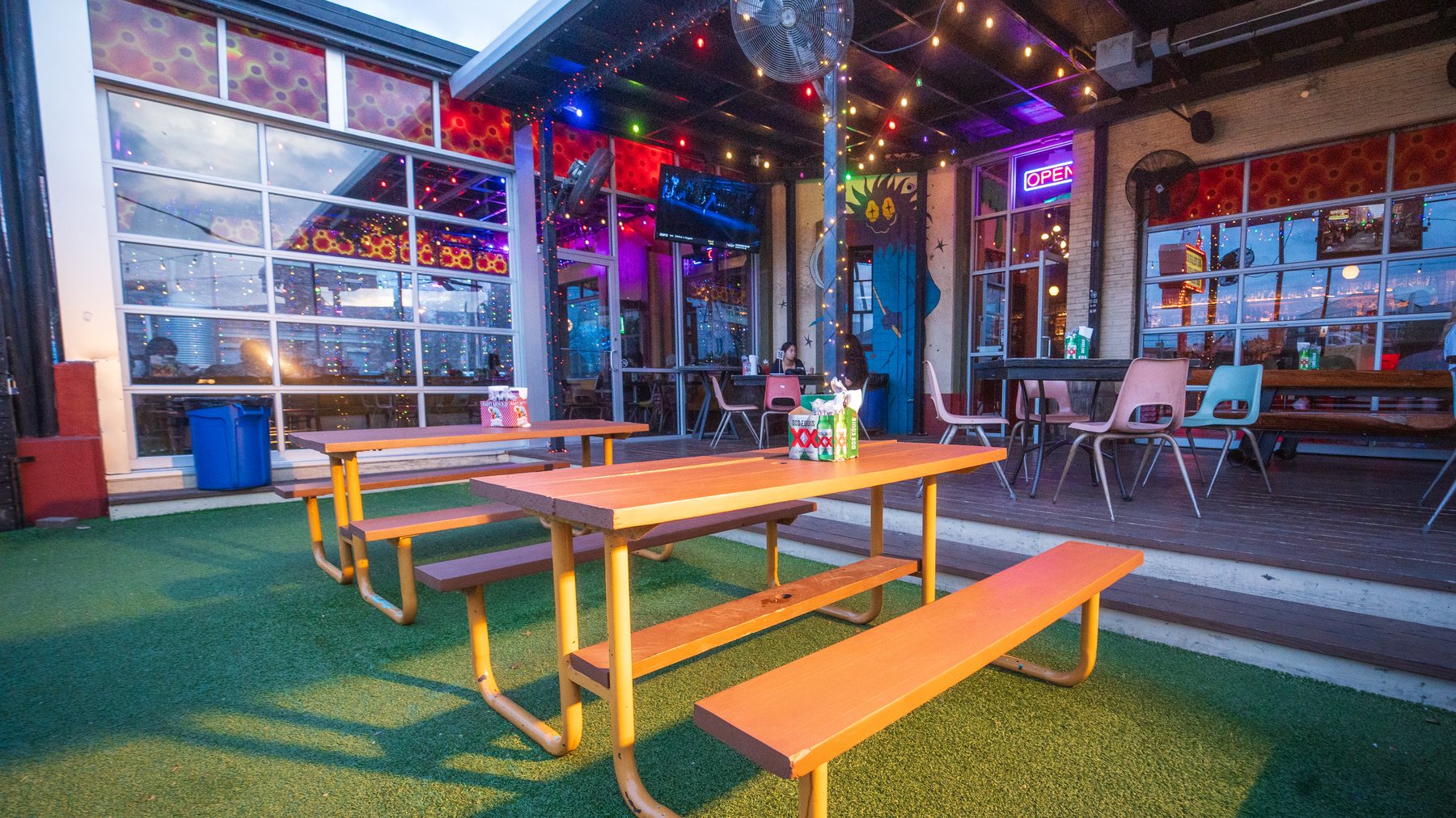 The Washington Ave patio at dusk: picnic tables on turf, string lights, the OPEN sign and the solarium windows
